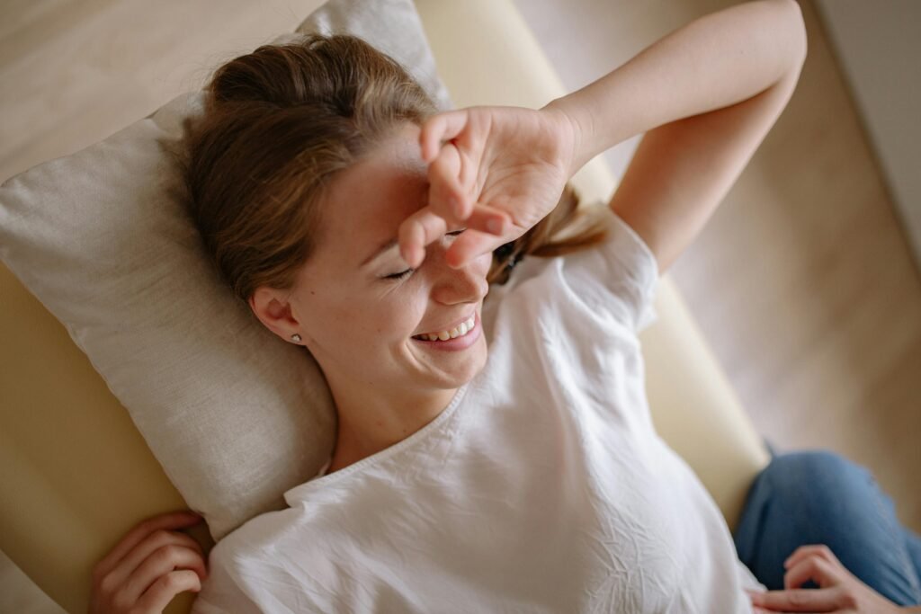 pexels-photo-5793975-5793975 Smiling woman in white top relaxing on bed with hand over face, enjoying leisure time.